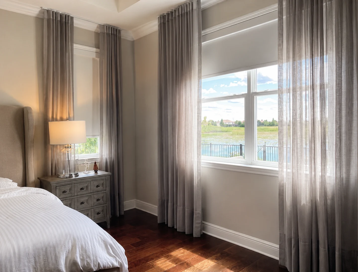 Quarto com cortinas cinza emoldurando a vista para um lago